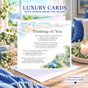 Thinking of You card with original verse, blue hydrangeas, birds and a countryside path, displayed with a white envelope beside a candle.