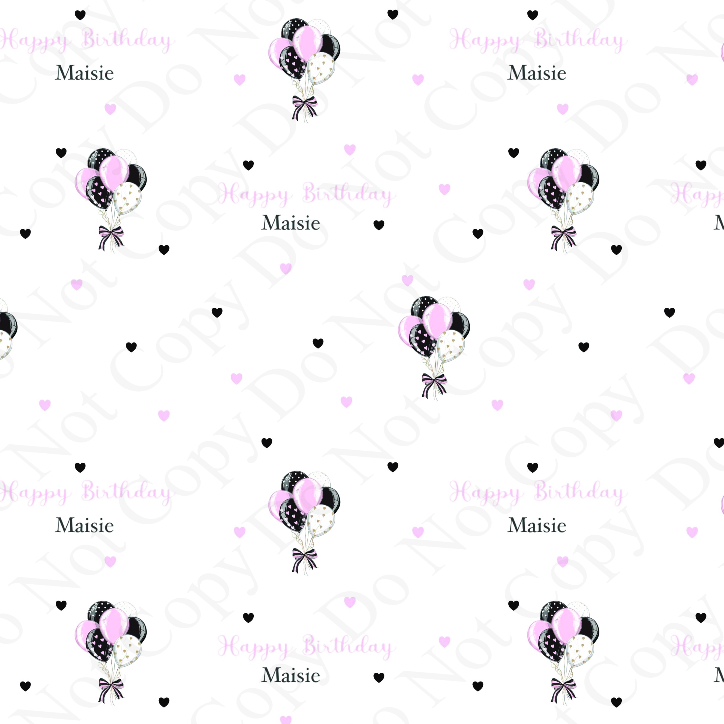 Close-up of personalised birthday wrapping paper featuring pink, black and white balloon bunches, scattered hearts and repeated “Happy Birthday Maisie” wording on a white background.